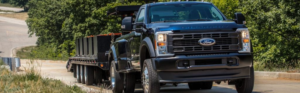 Black Ford Super Duty flatbed truck on a rural road.