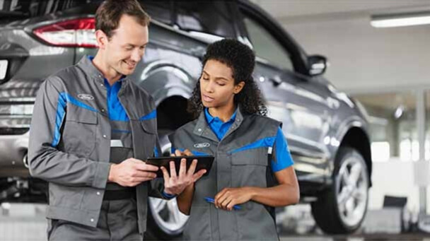 Two Ford technicians looking at a tablet in a service garage.
