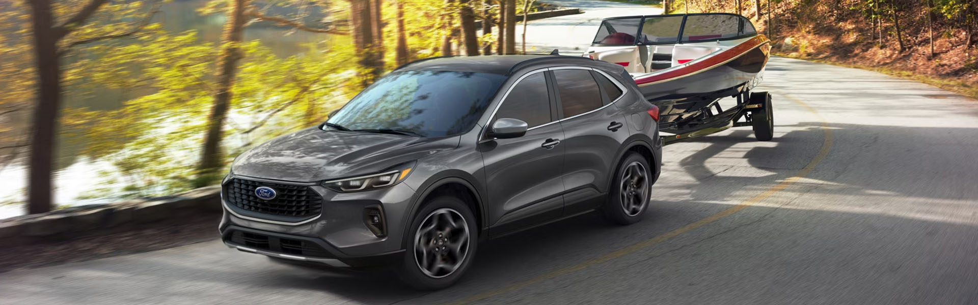 Dark gray Ford Escape SUV towing a speed boat on a winding road along a lake.